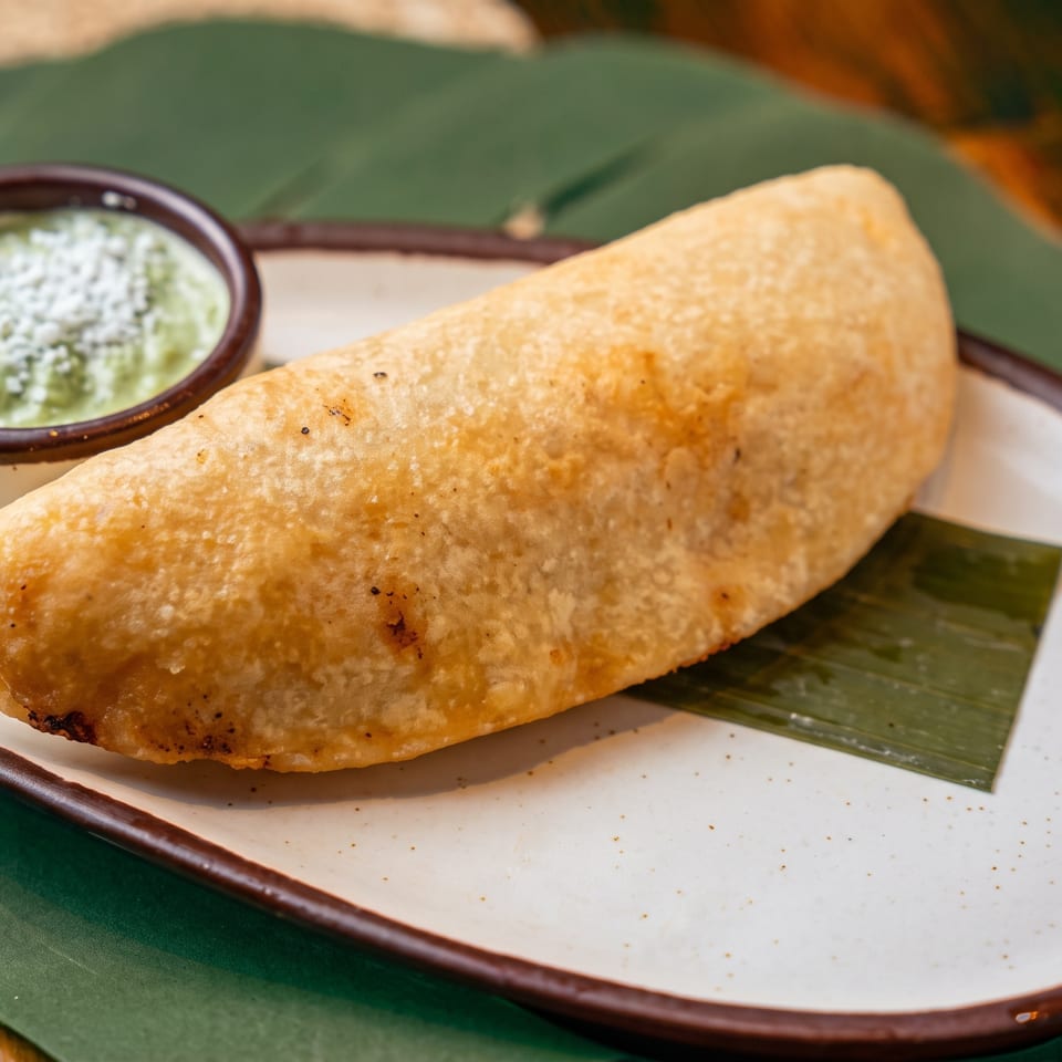 Golden folded dosa served on a plate with green chutney in a small bowl.