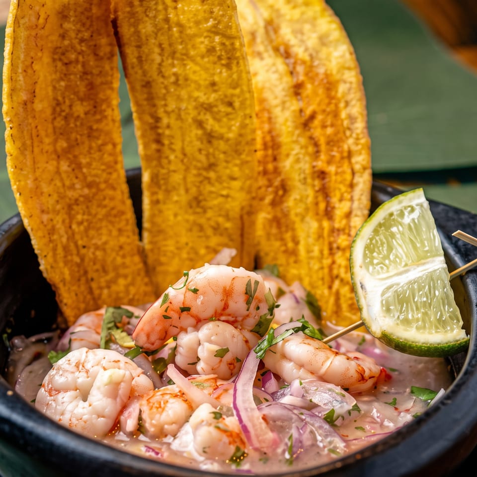 Shrimp ceviche with red onion, cilantro, lime wedge, and three golden tostadas in a black bowl.